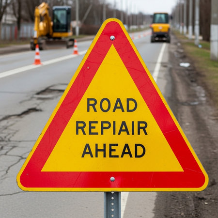 A warning sign indicates road repairs ahead, cautioning drivers of construction.の素材