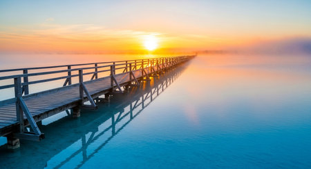 a serene sunrise over a wooden bridge extending into the calm ocean waterscapeの素材