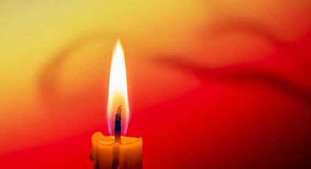 Burning candle on a red and yellow background, close-upの素材