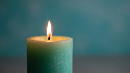 Close up of a burning green candle on blue background with copy spaceの素材