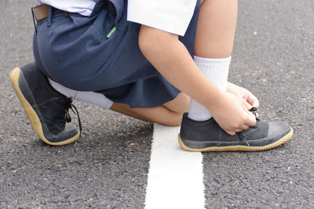 Childs student  tying shoes at roadside.の写真素材