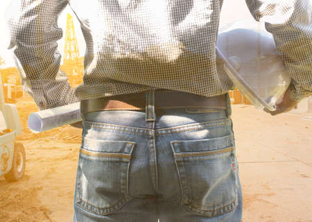 Man architect with white helmet and house plans his hand on background of site construction.の写真素材