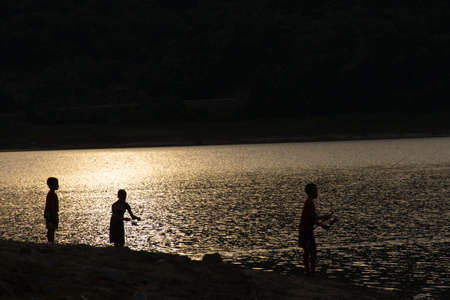 Children fishing by the lakeside and sunset view.の写真素材