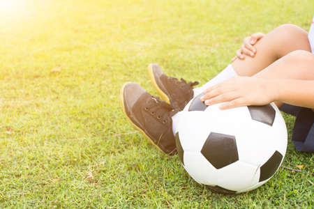 Boy is sitting on green grass with a soccer ball in his hand.Close upの写真素材