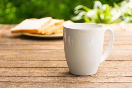 White coffee cup and bread slice on wooden table and nature background.の写真素材