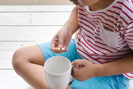 Sick child eating pills with wooden white background .Top viewの写真素材