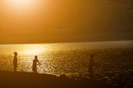 Children fishing by the lakeside and sunset view.の写真素材