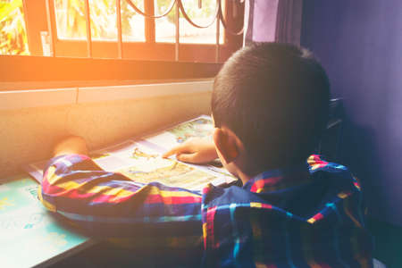Child reading book by the window in the library.Behind the child and Zoom in.の写真素材