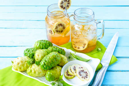 Noni fruit in the dish and noni slice  and noni juice with knife on green checkered fabric.Top viewの写真素材