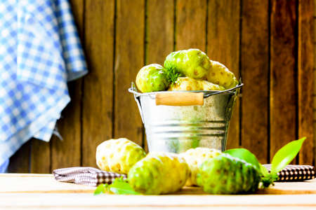 Noni fruit in zinc bucket and noni on table and old wooden background.の写真素材
