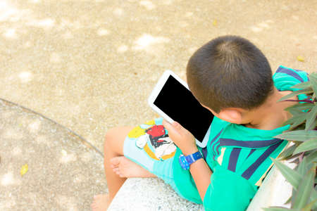 Child Asian using tablet computer in his hand in public park.の写真素材