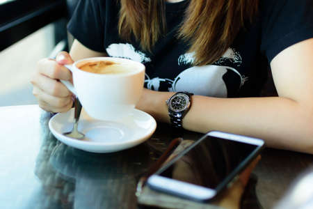 Woman with coffee cup in her hand with smartphone and etc on table.