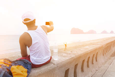 Young man taking photo by smartphone,Or American man with smartphone in his hand and the beach.