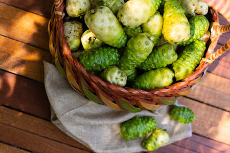 Noni basket and noni on Brown cloth on wooden table with nature background,Top view.