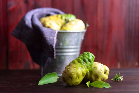 Noni fruit and leaves and noni in tank on wooden table.の写真素材