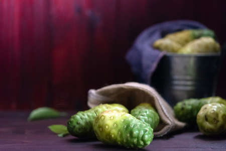 Noni in sack and  noni in tank and noni with leaves on wooden tableの写真素材
