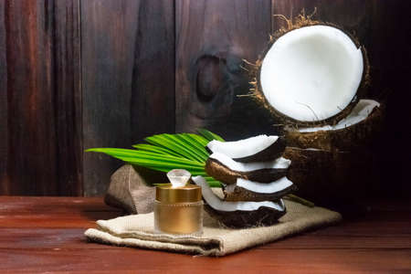 Face cream coconut oil and coconut half with coconut pieces and leaf on wooden background.の写真素材