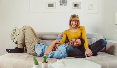 Happy young couple laughing having fun while talking on the sofa.の写真素材