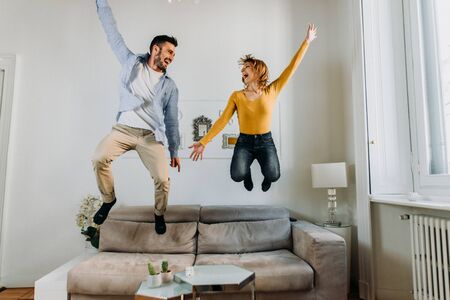 Happy couple in love having fun together jumping on the sofa in the living room at home.の写真素材