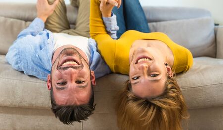 Happy couple is lying upside down on the sofa at home.の写真素材