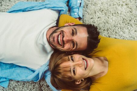 Portrait of a charming beautiful young couple in love lying on a gray carpet in the living room at home, holding each other face.の写真素材
