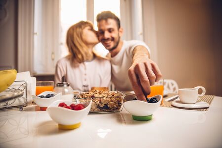 Young happy couple sitting by table having breakfast together at morning. Focus on the hand.の写真素材
