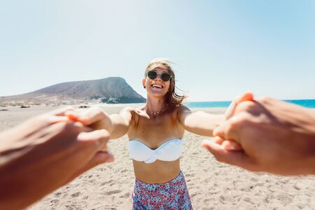 Smiling woman holding man's hand while walking on the beach