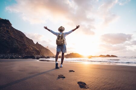 Young man arms outstretched by the sea at sunrise enjoying freedom and life, people travel wellbeing conceptの写真素材