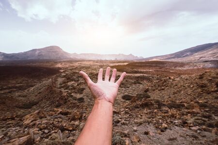 Hand of a man reaching out the beatiful mountain landscape at sunseの写真素材