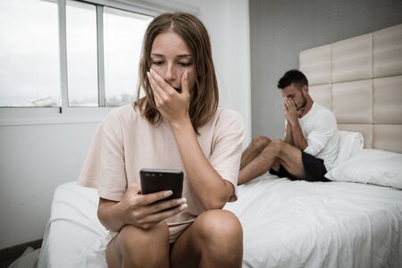 Sad woman finds out about her boyfriend's betrayal by spying on his phoneの写真素材