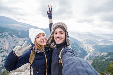 Happy beautiful couple of hikers taking a selfie on the top of the mountain. Two young people at vacation adventure in the nature smiling at the camera,の写真素材