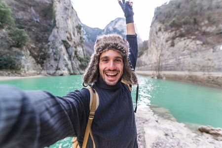 Happy traveler man takes a selfie photo on a lake at the mountain