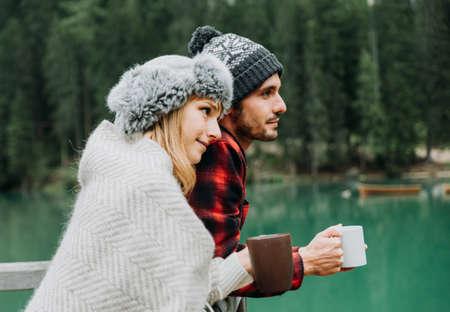 Couple of adults visiting an alpine lake at Braies Italy. Tourist in love drinking hot chocolate at autumn mountains. Couple, wanderlust and travel concept.の写真素材