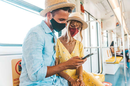 Young couple wearing face mask using smart phone - Young people checking online booking on the phone sitting on the train - Bright filterの写真素材