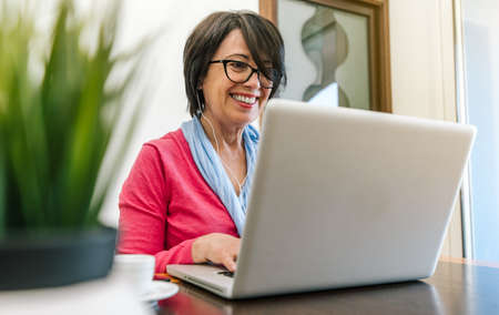 Senior older woman working with laptop computer on the table at home indoor. Old mature people and technology conceptの写真素材