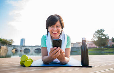 Senior woman training work out outdoor. Mature woman using fitness app doing sport. Senior people, fitness and technology concept.の写真素材