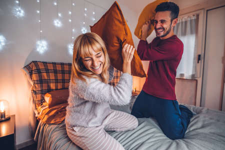 Couple having fun while pillow fight in the bed - Boyfriend and girlfriend enjoying the company of...