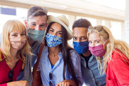 Portrait group of young happy friends wearing face mask during Covid pandemic smiling at the camera....