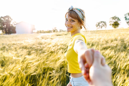 Woman holding boyfriend hands walking on a wheat field at sunsetの写真素材