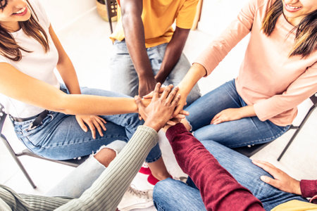 Close up of different people sitting on chairs in circle holding hands togetherの写真素材