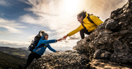 People helping each other hike up a mountain at sunriseの写真素材