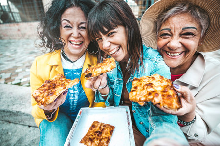 Three senior women eating pizza slice sitting outsideの写真素材