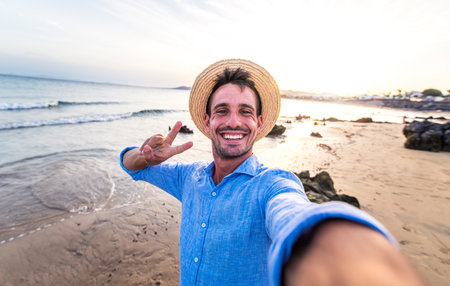 Handsome man taking a selfie at the beach - Portrait of a young happy guy outdoor smiling at cameraの写真素材