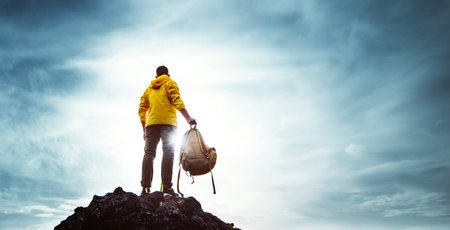 Young man with backpack standing on the top of a mountain at sunset - Goals and achievements