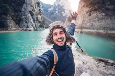 Handsome happy hiker taking a selfie on the top of the mountain - Smiling guy trekking outdoor at winterの写真素材