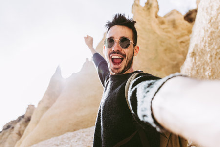 Happy young man wearing backpack hiking on a mountain taking a selfie with smartphone and action cam.の写真素材
