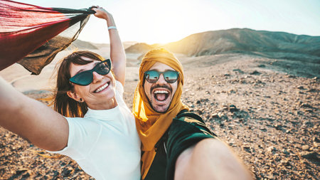 Happy couple of travelers taking selfie picture in rocky desert - Young man and woman having fun on summer vacationの写真素材