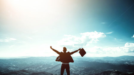 Silhouette of successful businessman keeping hands up hiking on the top of mountainの写真素材