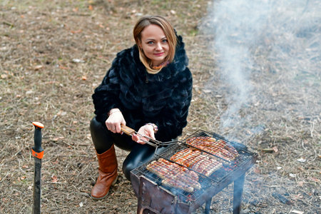 Beautiful woman fries sausages on the grill, early spring.の写真素材