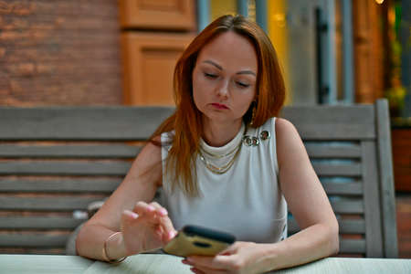 A woman in a restaurant is waiting for an order and looks into a smartphone.の写真素材